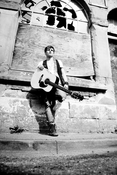 Young male musician standing on the street with his guitar