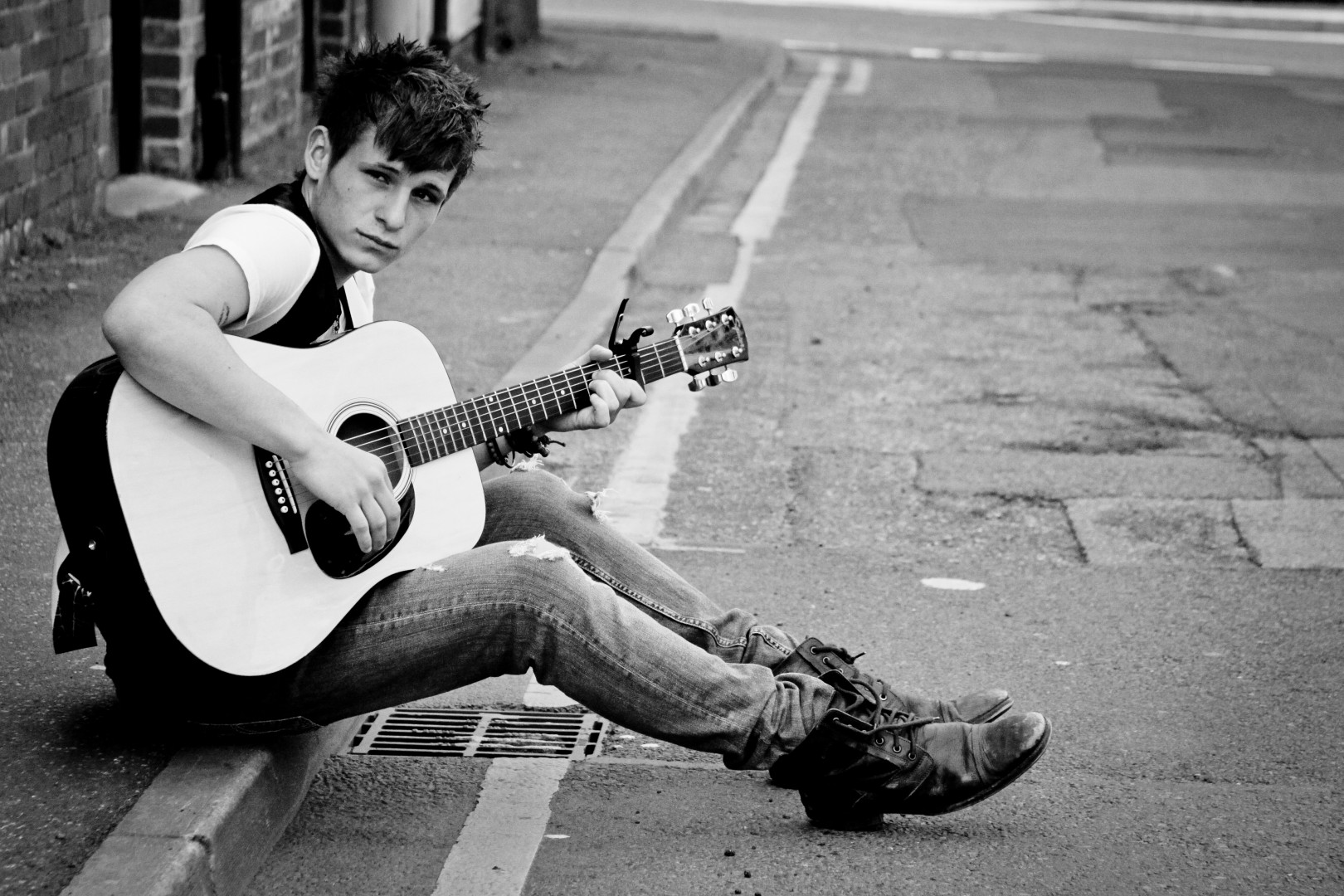 Young male musician sat on the pavement playing his guitar